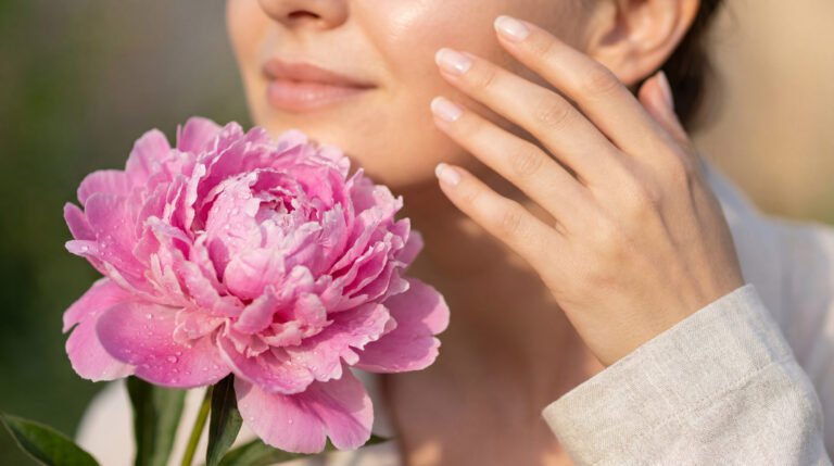 Une femme effleure délicatement son visage à côté d'une pivoine rose avec des gouttelettes d'eau.